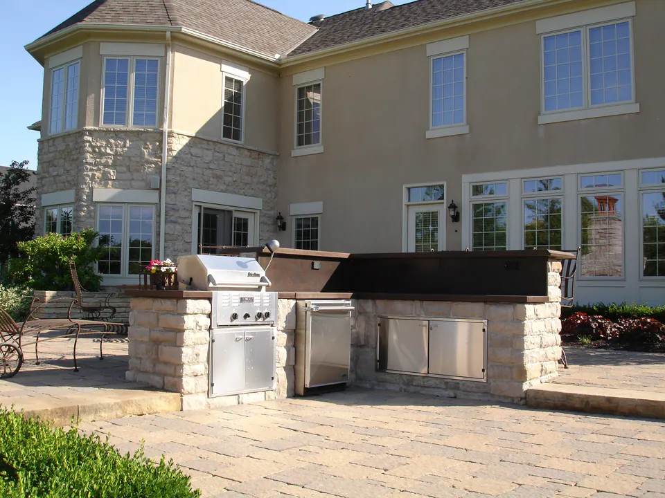Long stone outdoor kitchen island with grill, refrigerator and storage on a paver patio